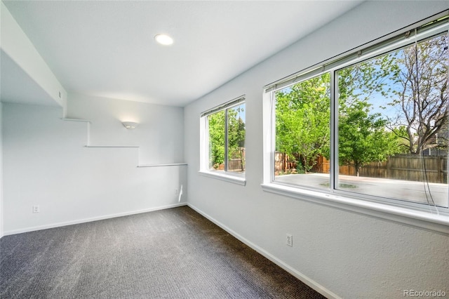 spare room with baseboards and dark carpet