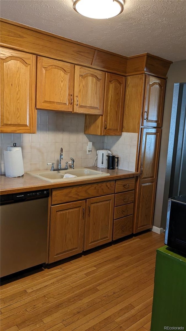 kitchen featuring tasteful backsplash, dishwasher, sink, and light wood-type flooring