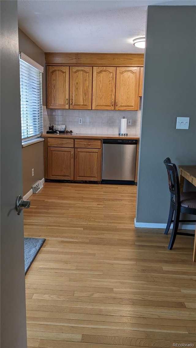 kitchen featuring stainless steel dishwasher, backsplash, and light wood-type flooring