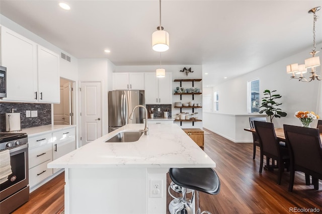 kitchen featuring a kitchen island with sink, white cabinetry, decorative light fixtures, and appliances with stainless steel finishes