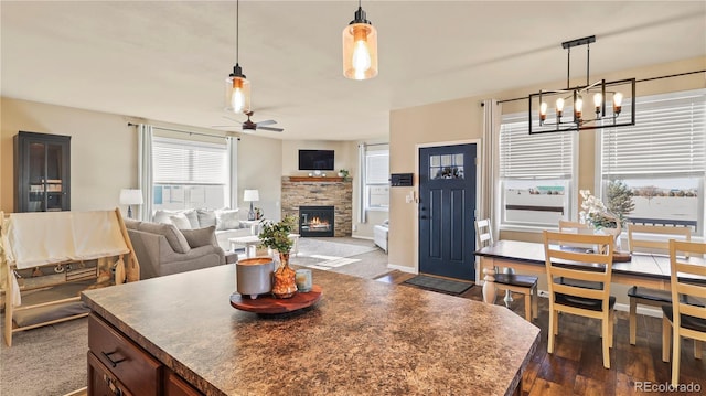 dining space featuring ceiling fan with notable chandelier, a stone fireplace, and dark wood-type flooring