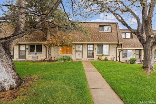 view of front of home featuring roof with shingles, brick siding, and a front yard