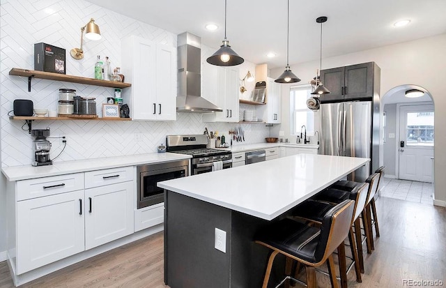 kitchen featuring tasteful backsplash, open shelves, wall chimney range hood, appliances with stainless steel finishes, and a sink