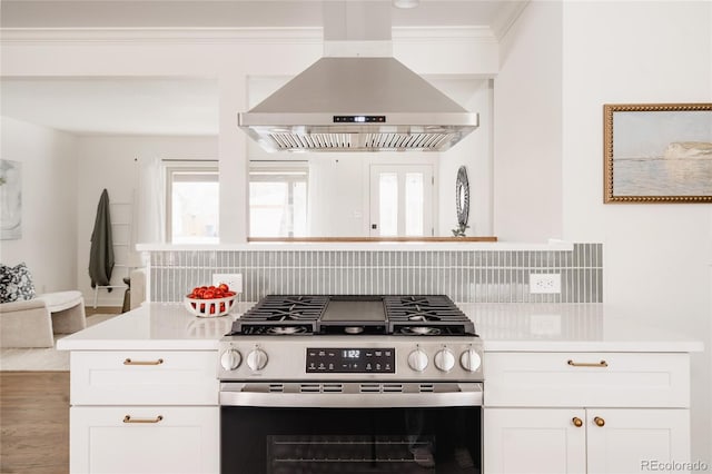 kitchen with wall chimney exhaust hood, stainless steel gas range oven, white cabinetry, and a healthy amount of sunlight