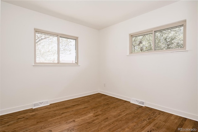 empty room featuring baseboards, dark wood finished floors, and visible vents