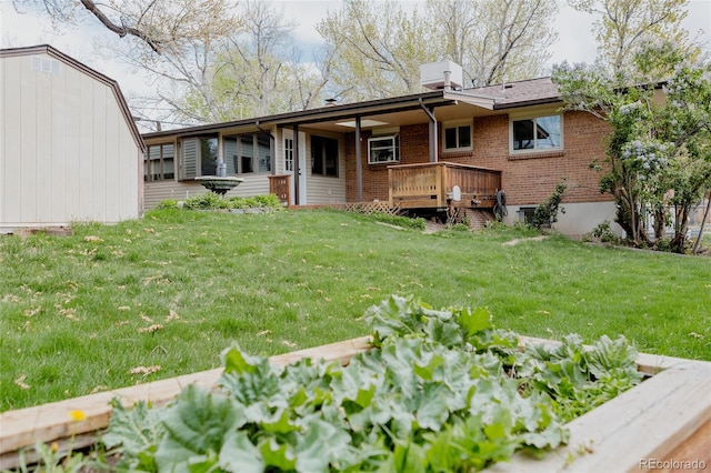 rear view of house featuring brick siding, a vegetable garden, a deck, a chimney, and a lawn