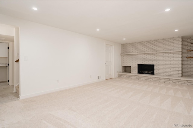 unfurnished living room with a brick fireplace, recessed lighting, baseboards, and light colored carpet