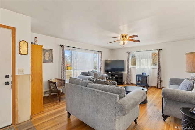 living room featuring ceiling fan, light hardwood / wood-style flooring, and a wood stove