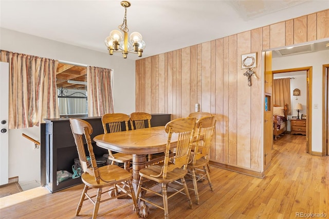 dining area featuring wooden walls, light hardwood / wood-style flooring, and a notable chandelier