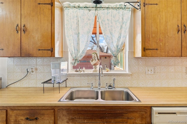 kitchen featuring dishwashing machine, sink, decorative backsplash, and hanging light fixtures