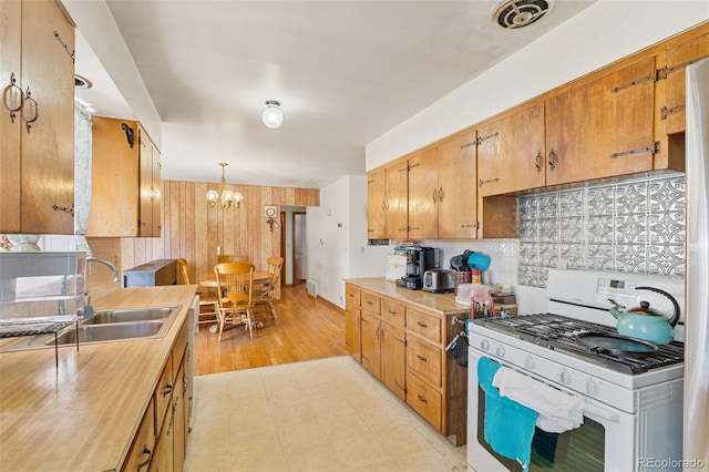 kitchen featuring pendant lighting, sink, gas range gas stove, decorative backsplash, and a chandelier