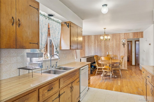 kitchen featuring decorative light fixtures, sink, backsplash, white dishwasher, and an inviting chandelier