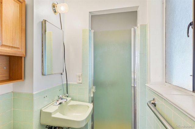 bathroom with a shower with door, sink, and tile walls