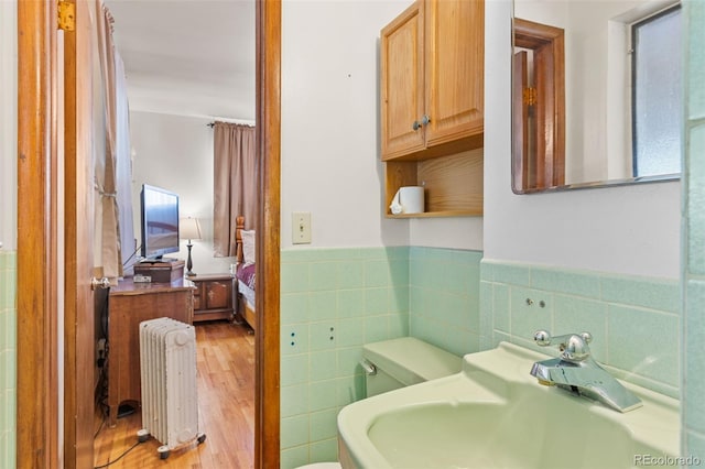 bathroom with tile walls, radiator, hardwood / wood-style floors, and sink