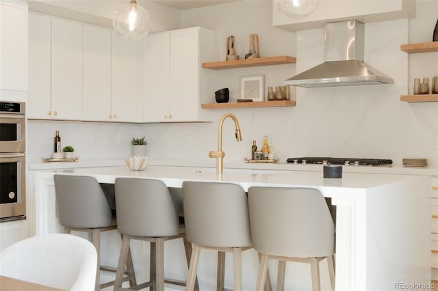 kitchen featuring a breakfast bar area, stainless steel appliances, wall chimney exhaust hood, and open shelves