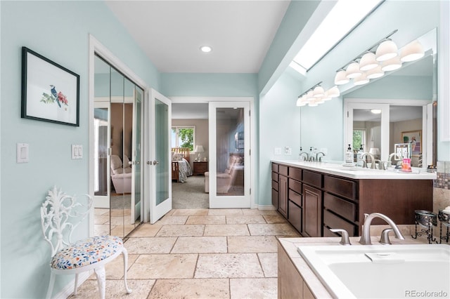 7330 Routt St, Arvada, CO 80005 - full bath featuring connected bathroom, french doors, double vanity, tiled tub, and stone tile floors