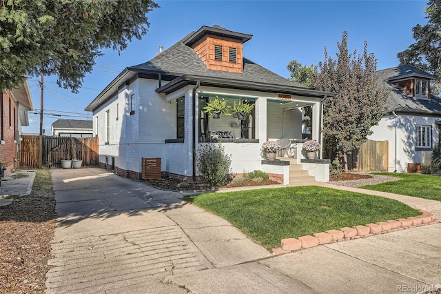 bungalow-style house with a front yard, fence, brick siding, and roof with shingles