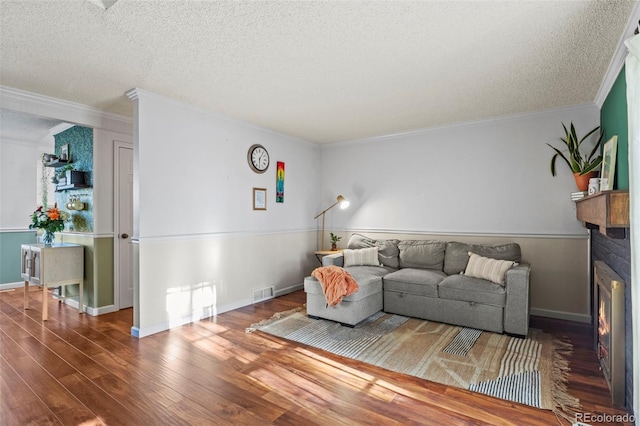 living area with a textured ceiling, wood finished floors, ornamental molding, a lit fireplace, and baseboards