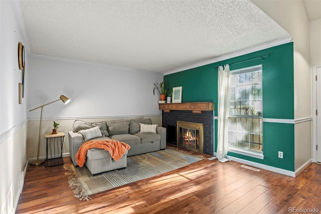 living area featuring a textured ceiling, a fireplace, wood finished floors, ornamental molding, and baseboards