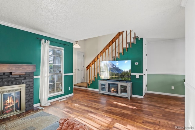 unfurnished living room with a brick fireplace, a textured ceiling, stairway, wood finished floors, and baseboards