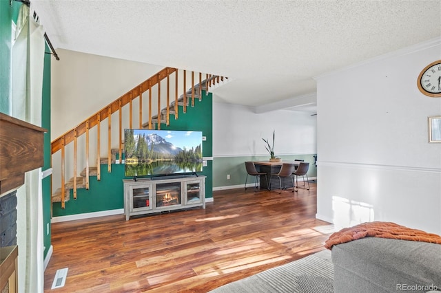 living area featuring wood finished floors, a fireplace, stairs, a textured ceiling, and ornamental molding