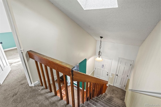 stairway featuring carpet flooring, a textured ceiling, baseboards, and lofted ceiling