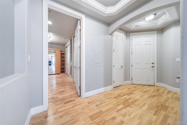 corridor with a raised ceiling, crown molding, and light hardwood / wood-style flooring