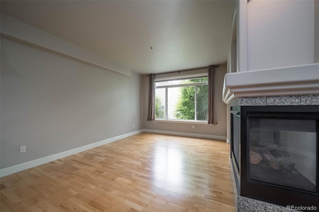 unfurnished living room featuring a tiled fireplace and light hardwood / wood-style flooring