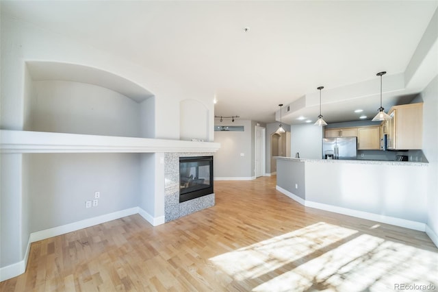 kitchen with light brown cabinets, light hardwood / wood-style flooring, stainless steel fridge, decorative light fixtures, and a tiled fireplace