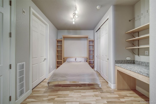 unfurnished bedroom featuring light hardwood / wood-style floors, rail lighting, and a closet