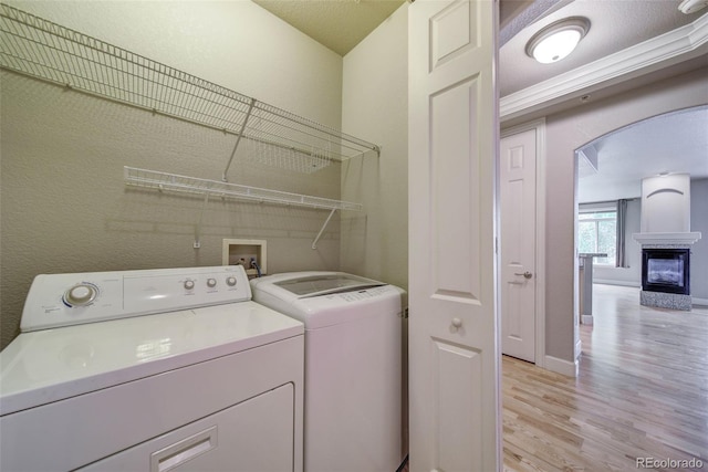 washroom featuring light wood-type flooring, a textured ceiling, crown molding, a multi sided fireplace, and independent washer and dryer