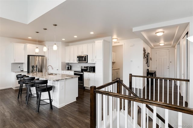11823 Barrentine Loop, Parker, CO 80138 - kitchen featuring appliances with stainless steel finishes, an island with sink, a kitchen breakfast bar, dark wood finished floors, and white cabinetry