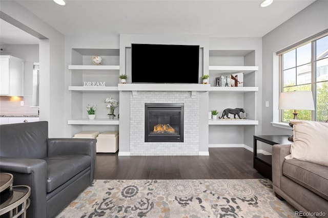 525 Grenville Cir, Erie, CO 80516 - living room with built in shelves, wood finished floors, a glass covered fireplace, baseboards, and recessed lighting