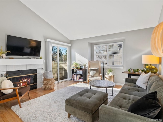 living room featuring vaulted ceiling, light hardwood / wood-style floors, and a tiled fireplace