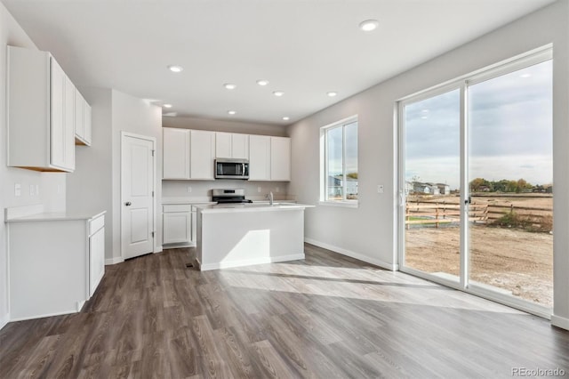 kitchen with stainless steel appliances, white cabinetry, wood-type flooring, and a kitchen island with sink