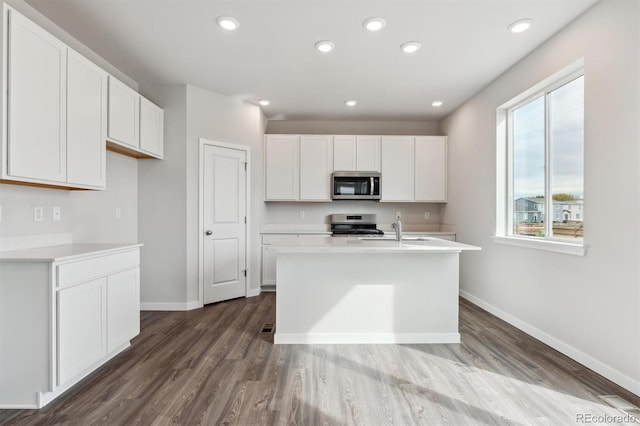 kitchen featuring sink, an island with sink, hardwood / wood-style flooring, stainless steel appliances, and white cabinets