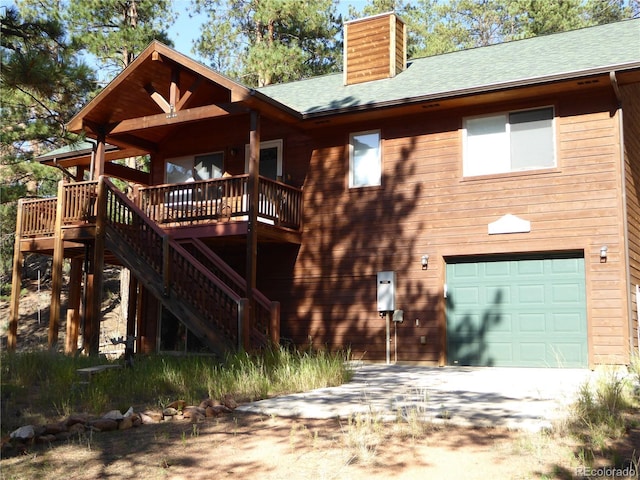 back of property featuring stairway, roof with shingles, a chimney, a deck, and an attached garage