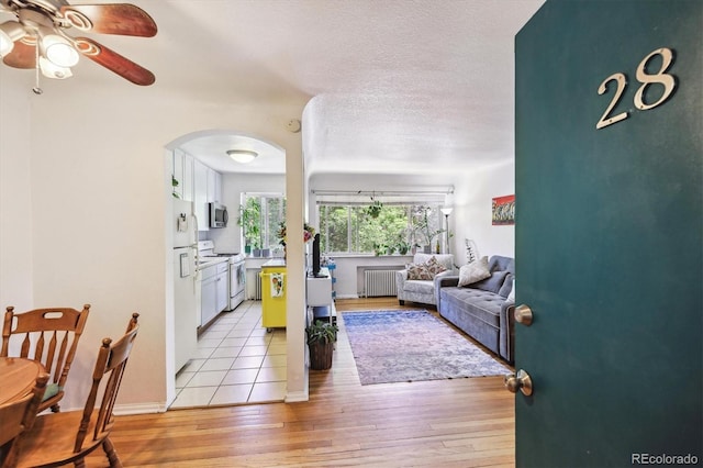 85 N Grant St Unit 28, Denver, CO 80203 - living room featuring radiator heating unit, arched walkways, ceiling fan, light wood finished floors, and a textured ceiling