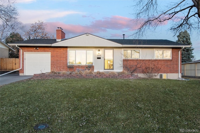 ranch-style house featuring a garage, a yard, a chimney, and brick siding