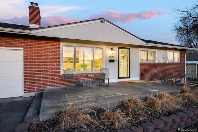 back of house at dusk featuring a chimney and brick siding