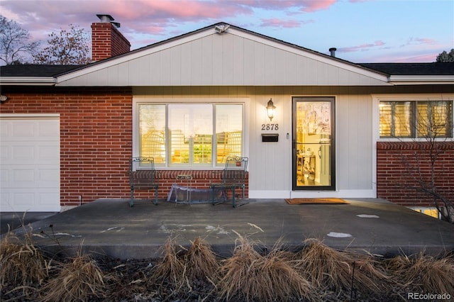 exterior entry at dusk with brick siding, a chimney, and an attached garage