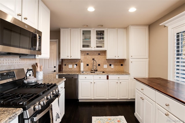 kitchen featuring white cabinets, wood counters, glass insert cabinets, stainless steel appliances, and a sink