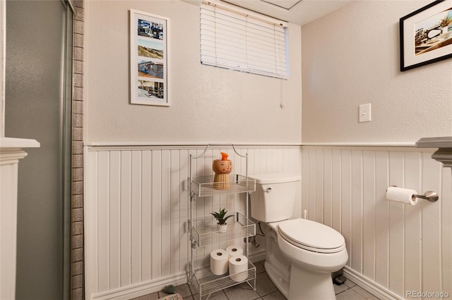 bathroom featuring tile patterned flooring, wainscoting, and toilet