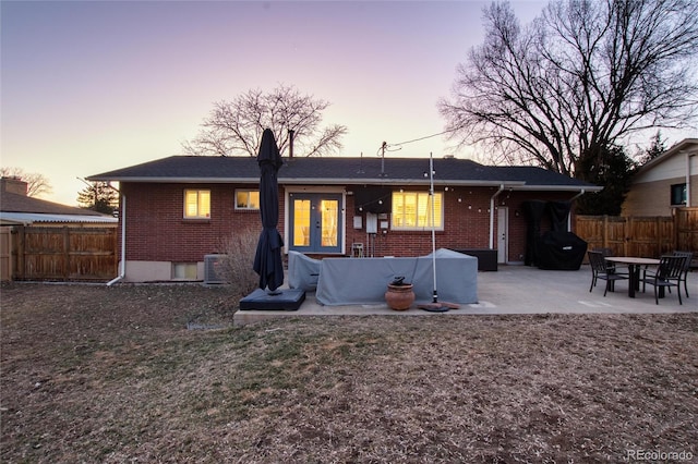 rear view of property featuring a patio, brick siding, a fenced backyard, and french doors