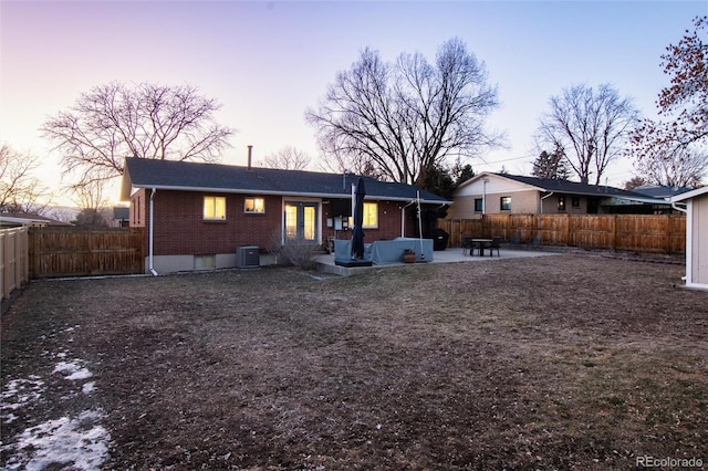 rear view of property with a fenced backyard, french doors, a patio area, central AC, and brick siding