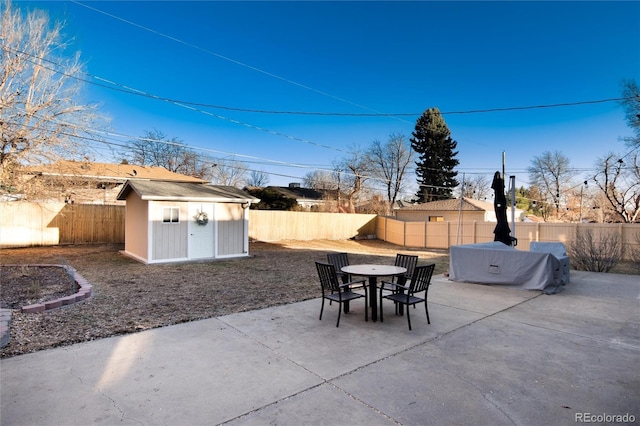 view of patio / terrace with a fenced backyard, a storage unit, an outbuilding, and outdoor dining space