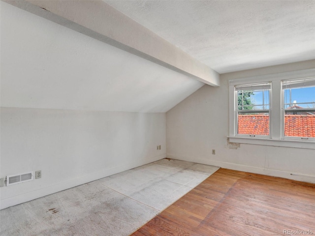 bonus room featuring vaulted ceiling with beams, light hardwood / wood-style floors, and a textured ceiling