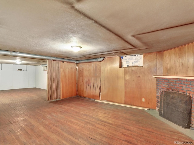 basement featuring a brick fireplace, hardwood / wood-style floors, and wooden walls