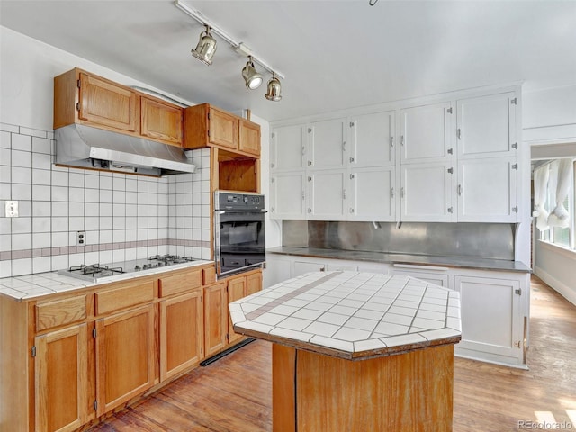 kitchen featuring a center island, gas stovetop, tile counters, oven, and light wood-type flooring