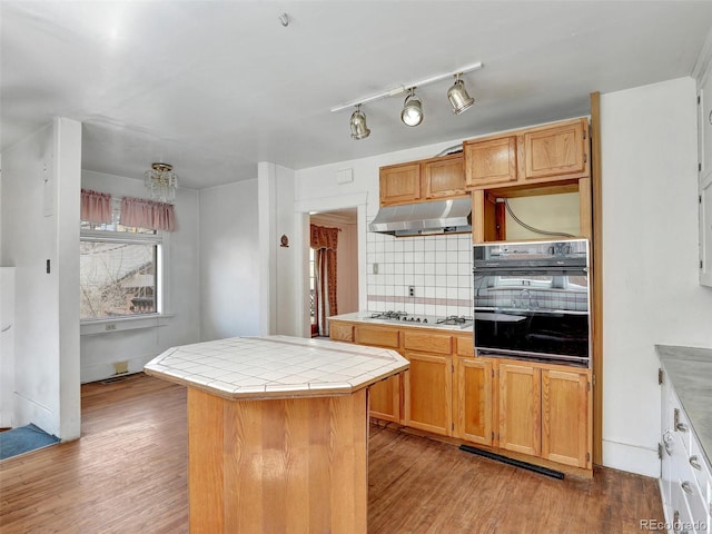 kitchen with tile countertops, black oven, a center island, gas stovetop, and light wood-type flooring